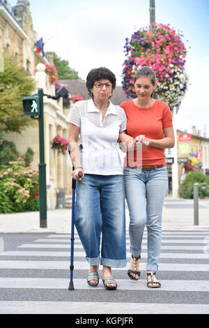 Casa cuidador ayudar a mujer mayor cruzando la calle Foto de stock