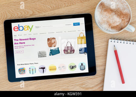 Características de la página web de eBay en un dispositivo tablet iPad que descansa sobre una mesa de madera junto a un bloc de notas y lápiz y una taza de café (uso Editorial solamente) Foto de stock