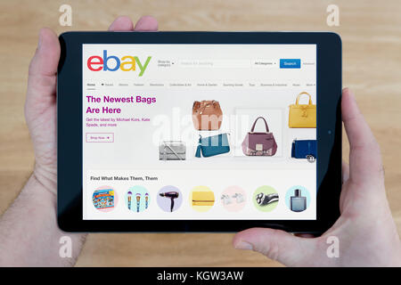 Un hombre mira la página web de eBay en su iPad dispositivo tablet, disparó contra una mesa de madera fondo superior (uso Editorial solamente) Foto de stock