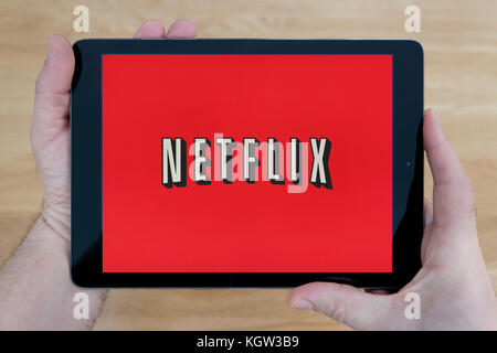 Un hombre mira la Netflix iPad app en su dispositivo tablet, disparó contra una mesa de madera fondo superior (uso Editorial solamente) Foto de stock
