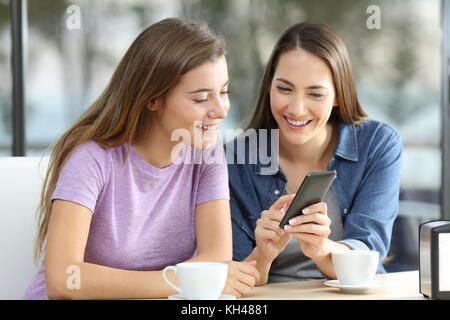 Dos amigos feliz compartir contenido en línea con un teléfono inteligente en un coffee shop