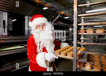 Santa Claus Baker con una bandeja de pastelitos de Navidad en sus manos