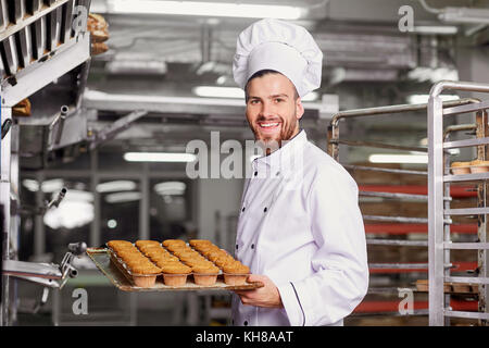 Un hombre panadero con una bandeja de pastelitos.