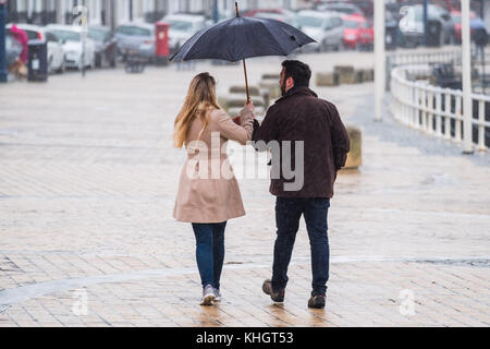 Aberystwyth Wales UK, Saturday 18 Novemberr 2017 UK Weather: Una pareja refugiándose bajo su paraguas compartido mientras caminan por el paseo marítimo en una mañana gris, nublada, húmeda y lluviosa en Aberystwyth Wales UK Foto © Keith Morris / Alamy Live News Foto de stock