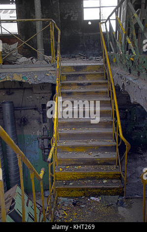 Escalera con pasamanos de color amarillo en las ruinas del interior. industrial antigua fábrica olvidada. Foto de stock