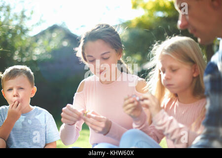 El padre y los hijos, sentados en el jardín, comer dulces