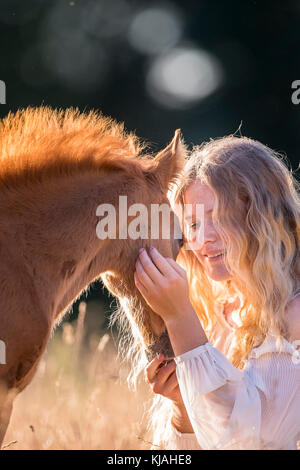 Alemán Caballo Pony. Chica smooching con la potra castaña-foal en luz del atardecer. Alemania Foto de stock