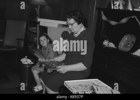 Abuela en un vestido azul sentarse erguido y jugando con un juego de mesa de mármol durante una fiesta, mientras que su nieta mira, 1963.