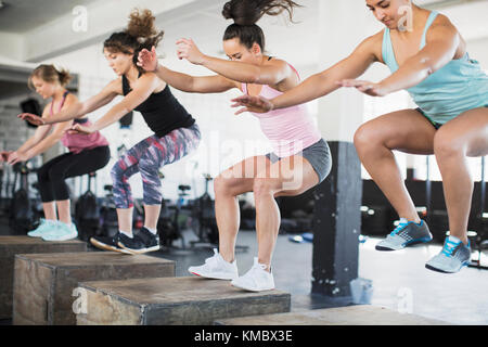 Determinadas mujeres haciendo sentadillas de salto en las cajas en la clase de ejercicio Foto de stock