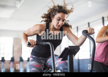 Determinada mujer joven montando bicicleta elíptica en el gimnasio Foto de stock