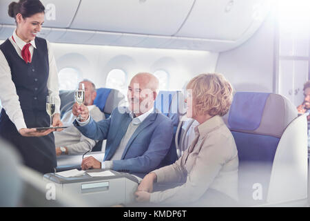 El asistente de vuelo sirve champán a una pareja madura en primera clase en avión Foto de stock