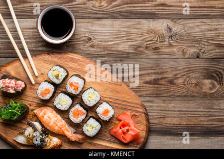 Sushi, rollos y especias sobre fondo de color marrón claro de madera Foto de stock
