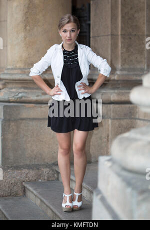 Retrato de una joven mujer vistiendo una chaqueta blanca y vestido negro con blanco zapatos con plataforma través de la histórica arquitectura columnas antecedentes de stock - Alamy