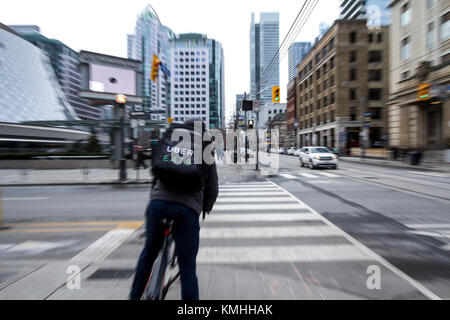 TORONTO, Canadá - 31 de diciembre de 2016: Uber come hombre entrega sobre una bicicleta esperando para cruzar una calle en el centro de Toronto, Ontario, con un movimiento bl Foto de stock