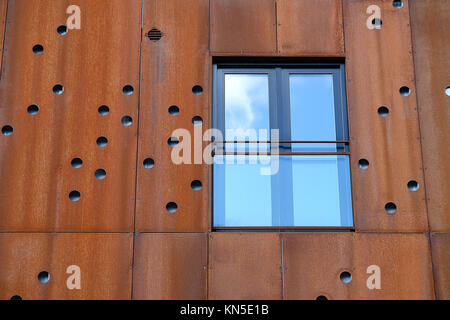 Primer plano de una ventana con balcón francés en fachada de edificio con placas de metal oxidado con orificios redondos Foto de stock