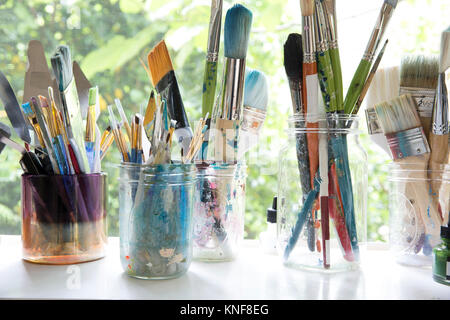 Fila de frascos con variedad de pinceles de artista sobre el alféizar de la ventana de artistas studio Foto de stock
