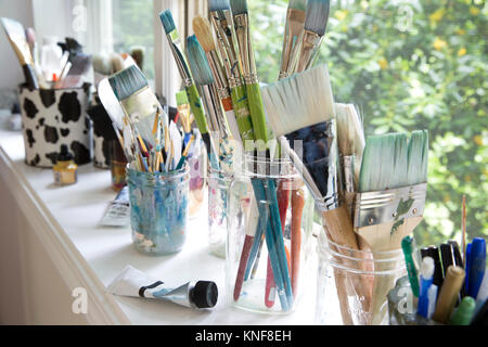 Fila de frascos con variedad de pinceles de artista sobre el alféizar de la ventana de artistas studio Foto de stock