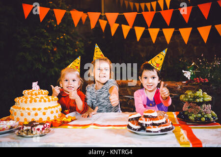 Fiesta de cumpleaños de niños. Tres niños alegres chicas comiendo torta con sus manos y las manchas de su rostro. Diversión y humor festivo en el decorado c