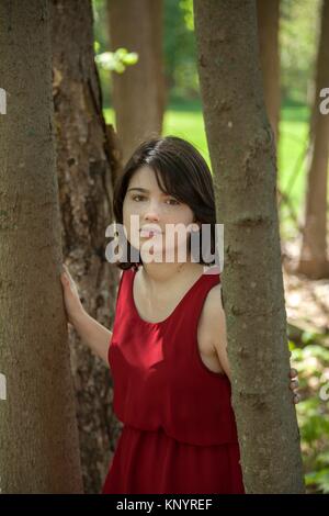 Mujer joven, de pie por los árboles en un parque, llevaba un vestido rojo.