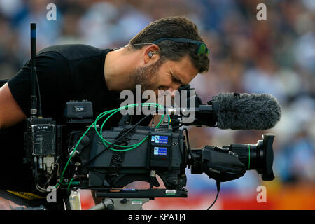 Un hombre de cámara de televisión filmando en un estadio deportivo.