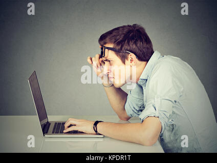 Hombre joven que tenía problemas de visión mirando perplejos mientras ve la laptop. Foto de stock