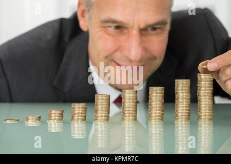 Empresario colocando Moneda a pila de monedas en el escritorio Foto de stock