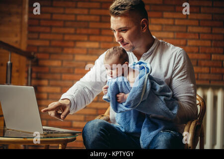 El padre con el bebé recién nacido trabaja desde casa con el portátil