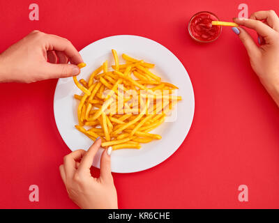 Mujer sumergiendo papas fritas en mayonesa sobre fondo rojo