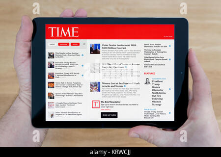 Un hombre se ve en el sitio web de la revista Time en su iPad dispositivo tablet, disparó contra una mesa de madera fondo superior (uso Editorial solamente) Foto de stock