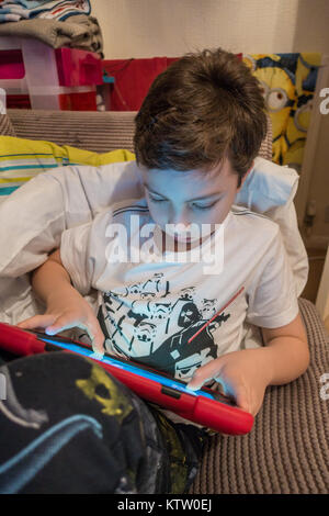 Un joven, vestida en pijama, se relaja en un sofá playigng en su iPad. Foto de stock