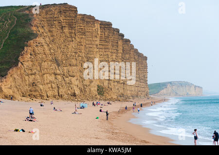 Turistas en la playa bajo el acantilado en West Bay, Dorset, Inglaterra, Reino Unido Foto de stock