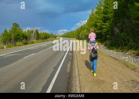 Dos hermanas vaya por la carretera, de vuelta a la cámara, en la naturaleza, en los meses de verano Foto de stock