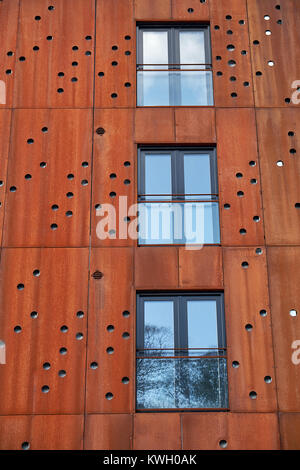 Primer plano de ventanas francesas con balcones en la fachada de edificio con placas de metal oxidado con orificios redondos