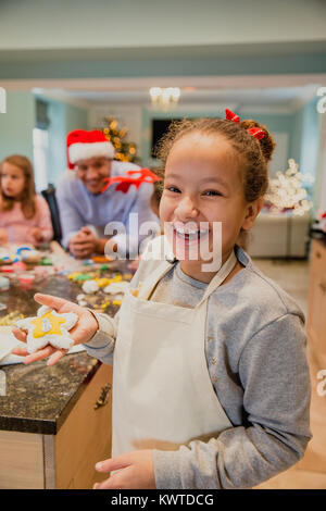 Orgullosa niña posando para la cámara con una galleta de navidad que ha hecho con su familia en casa. Foto de stock