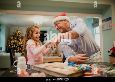 Niña es divertirse haciendo galletas de Navidad con su papá. Él es alegremente moviendo el azúcar en polvo en ella. Foto de stock