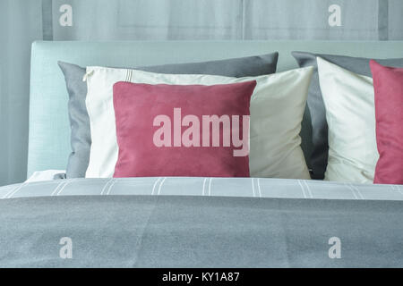 Almohadas de terciopelo rojo con blanco y gris de las almohadas en la cama en el esquema de color gris Foto de stock