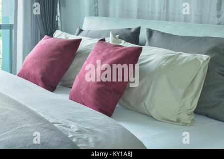 Almohadas de terciopelo rojo con blanco y gris de las almohadas en la cama en el esquema de color gris Foto de stock