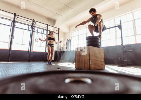 Colocar cuadro joven mujer saltando con ejercicio con cuerdas de saltar en un estilo cross training gimnasio. Pareja durante una intensa sesión de ejercicio físico en la salud clu Foto de stock