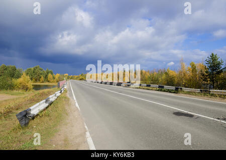 El asfalto de carretera a través del bosque de otoño. Nubarrones Foto de stock