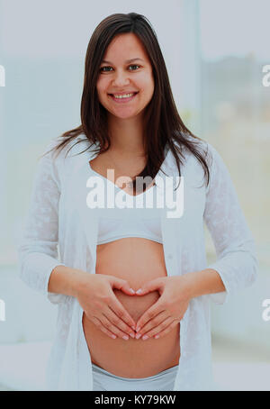 Mujer embarazada muestra el corazón de su bebé bump por manos. Foto de stock