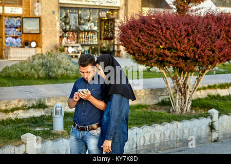 Isfahan, Irán - 23 de abril de 2017: una joven pareja pasea por Naghsh e Jahan Plaza, y mira algo en la pantalla del smartphone. Foto de stock