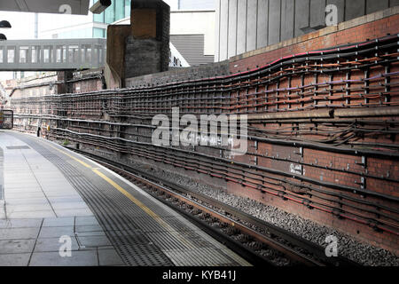 Plataforma vacía y la vía del tren en la línea de ferrocarril con infraestructura de cables visibles en pared de ladrillo en la estación de tren en Londres England Reino Unido. Kathy DEWITT Foto de stock