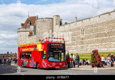 Open-top sightseeing bus rojo estacionado fuera de la muralla y la torre del castillo de Windsor vistos desde el centro de la ciudad en un día soleado de verano, Windsor, REINO UNIDO