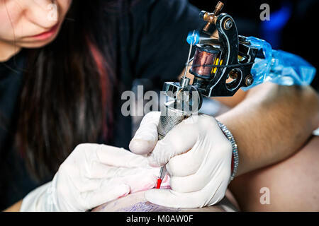 Cerrar las manos con la máquina haciendo tatuajes de aves en fémur de mujer Foto de stock