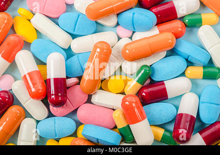 Las tabletas y cápsulas de coloridas píldoras montón de medicina sobre fondo azul.