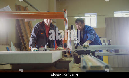 Los trabajadores carpinteros están cortando tablón de madera de la sierra eléctrica en la fábrica de muebles Foto de stock