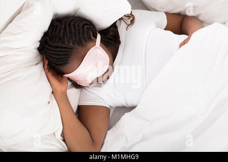 Close-up de una muchacha africana con máscara de ojo rosa durmiendo en cama