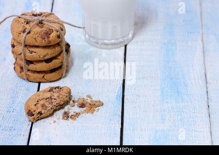 Pila de galletas con trocitos de chocolate con un vaso de leche fresca en la mesa de madera azul