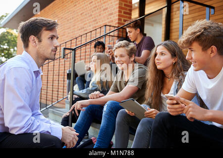 Los estudiantes adolescentes hablando con el profesor fuera de edificios escolares