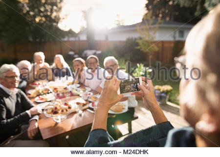 Mujer de más edad con cámara teléfono fotografiar amigos disfrutando garden party en el soleado patio tabla